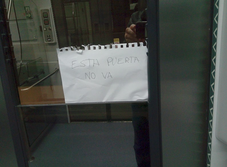 En la imagen el interior de un tren de cercanías con un cartel escrito a mano "Esta puerta no va"